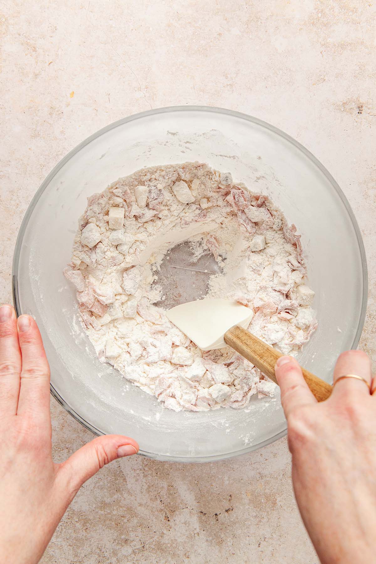 A hand using a rubber spatula to make a well in the middle of a bowl of dry ingredients.