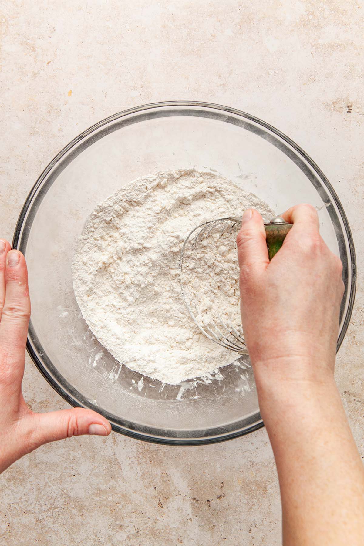 A hand using a pastry blender to mix butter into a bowl of dry ingredients.