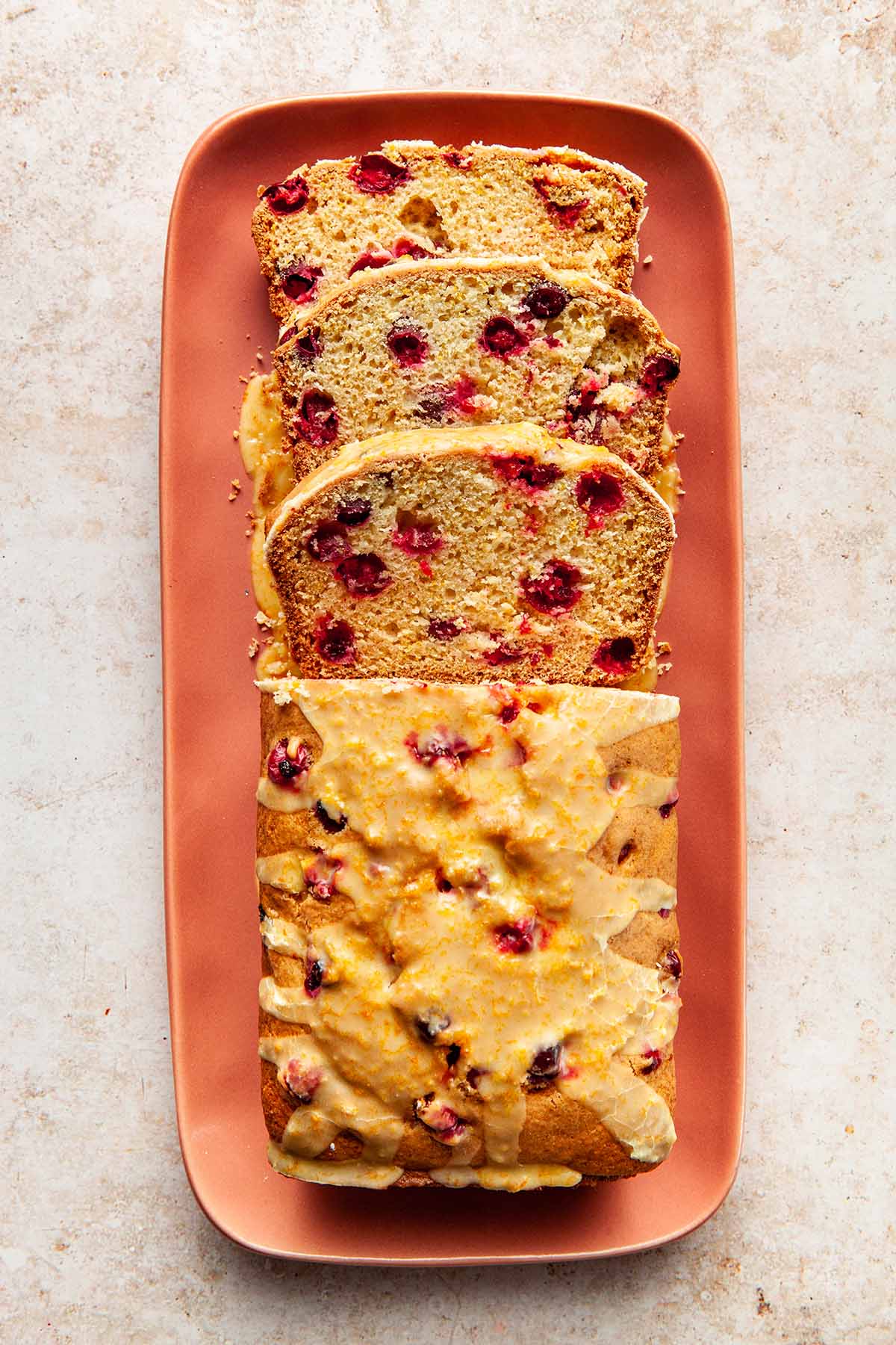 A half-sliced cranberry orange loaf on a coral-pink rectangle platter with rounded corners.