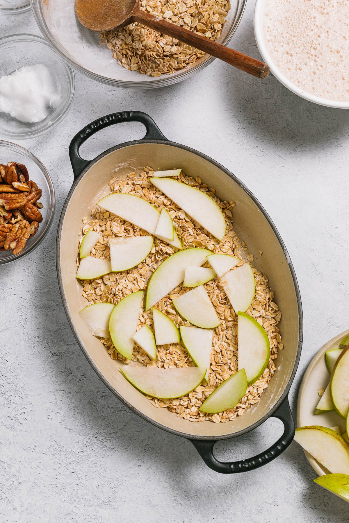 A baking dish with uncooked oats topped with sliced pear.