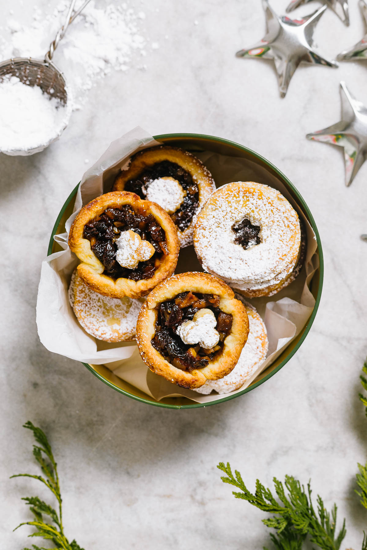 Mincemeat tarts in a tin with Christmas decorations around.