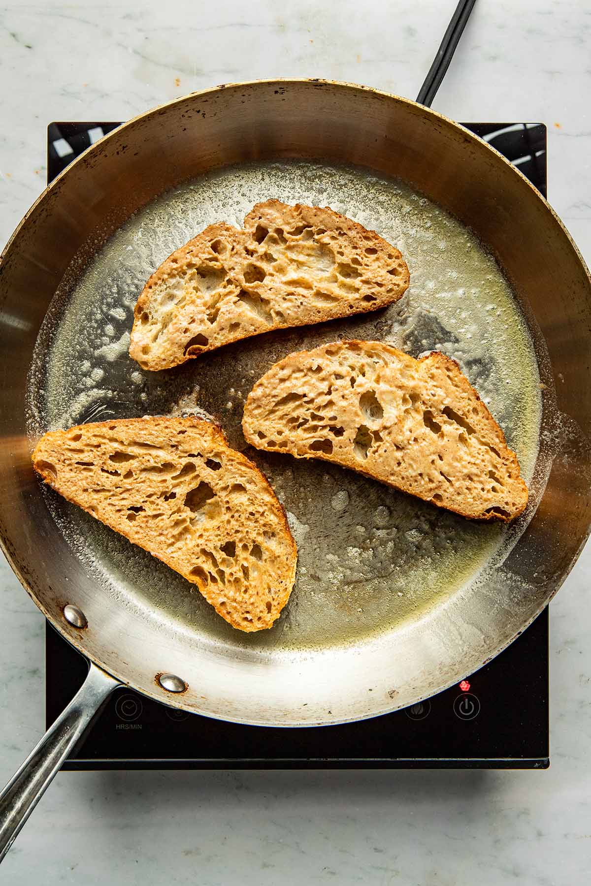 Three slices of bread in a buttered frying pan.