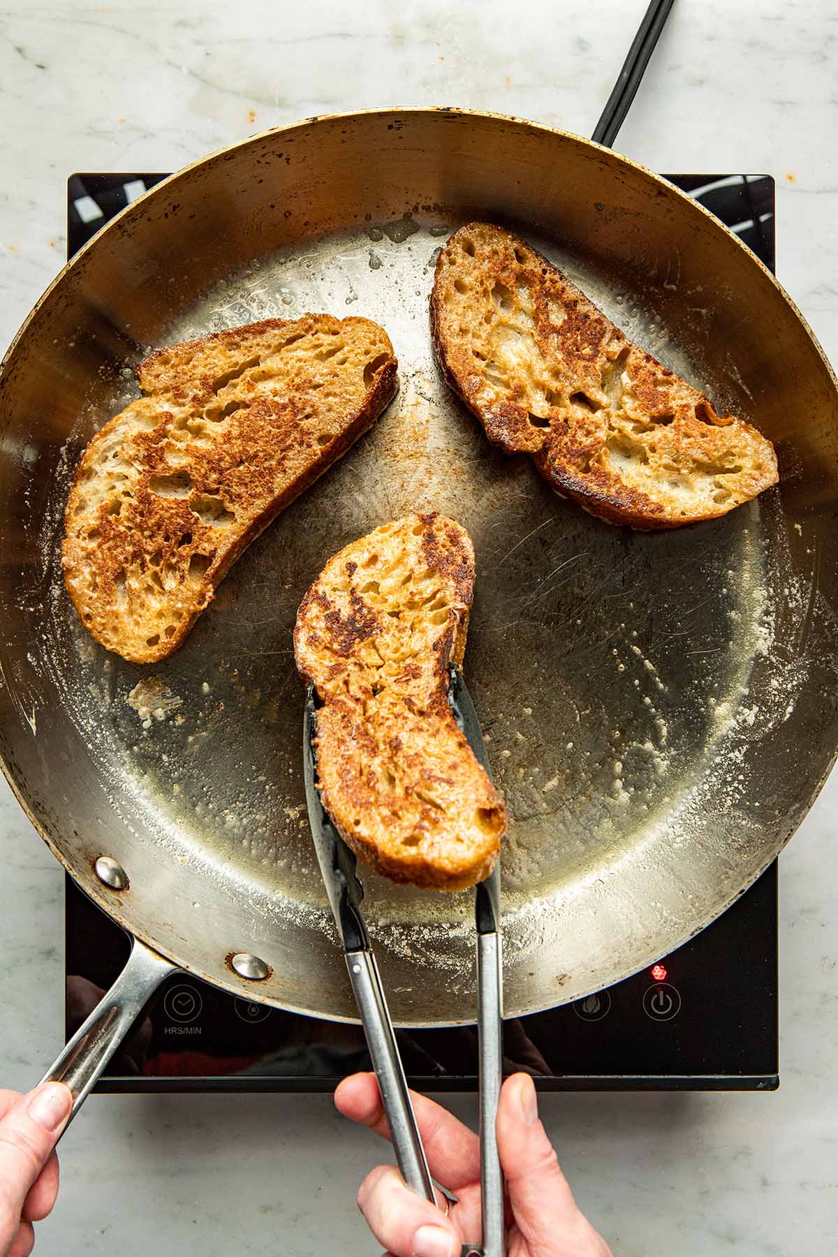 A hand using a pair of tongs to flip bread over in a frying pan.