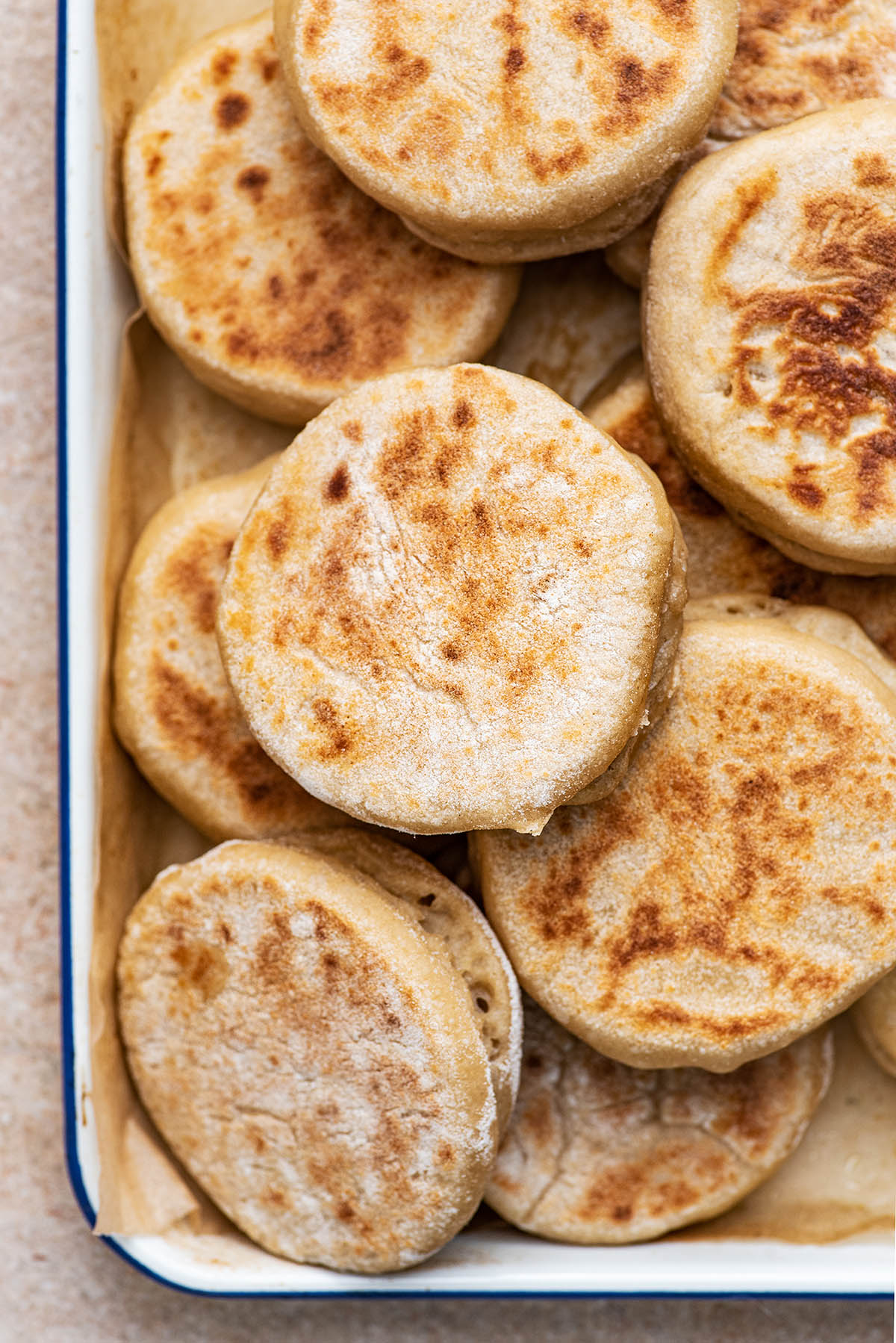 A pile of English muffins in a shallow tray.