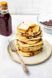 A stack of several chocolate chip pancakes with butter.