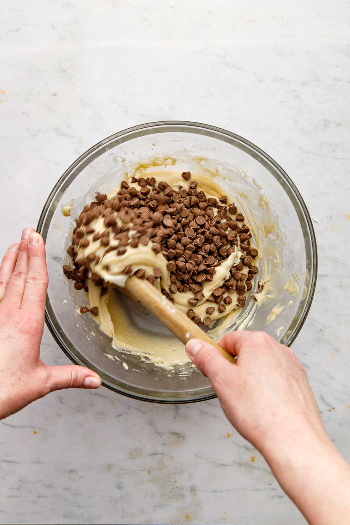 A hand folding chocolate chips into cake batter using a rubber spatula.