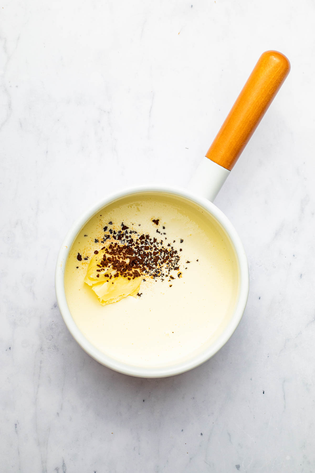 Cream, butter, and espresso powder in a small white pot.