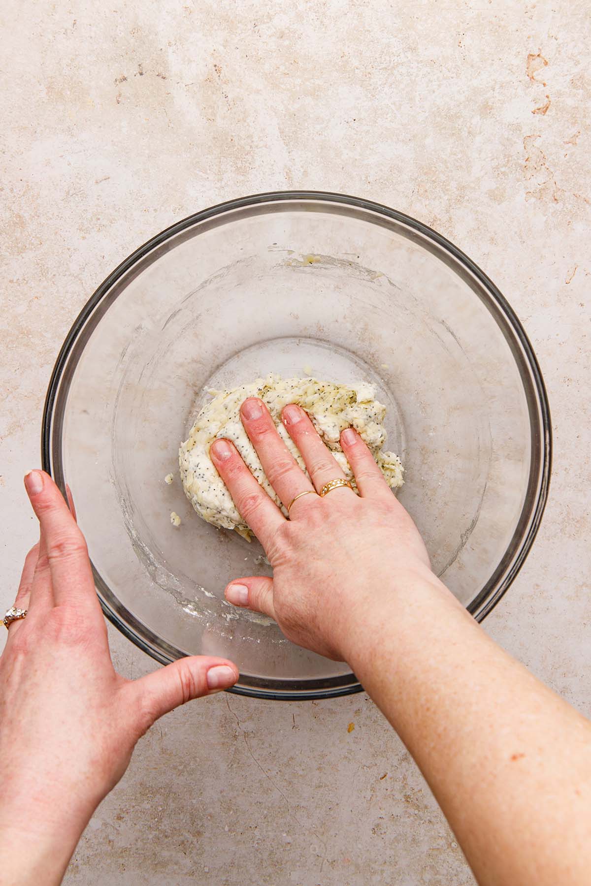 Hands lightly kneading dough in a glass bowl.
