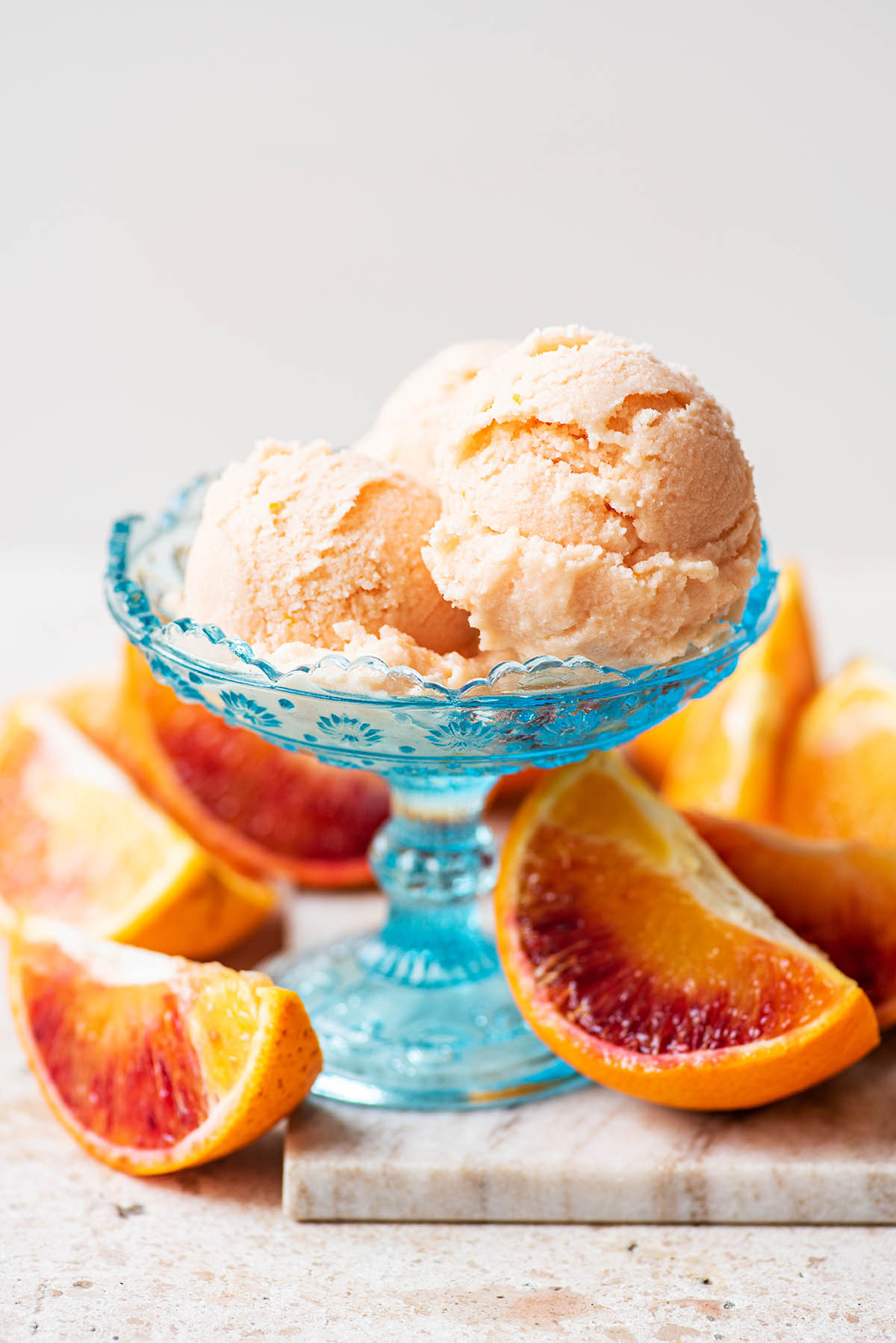 Three scoops of sherbet in a coupe glass with orange slices around.