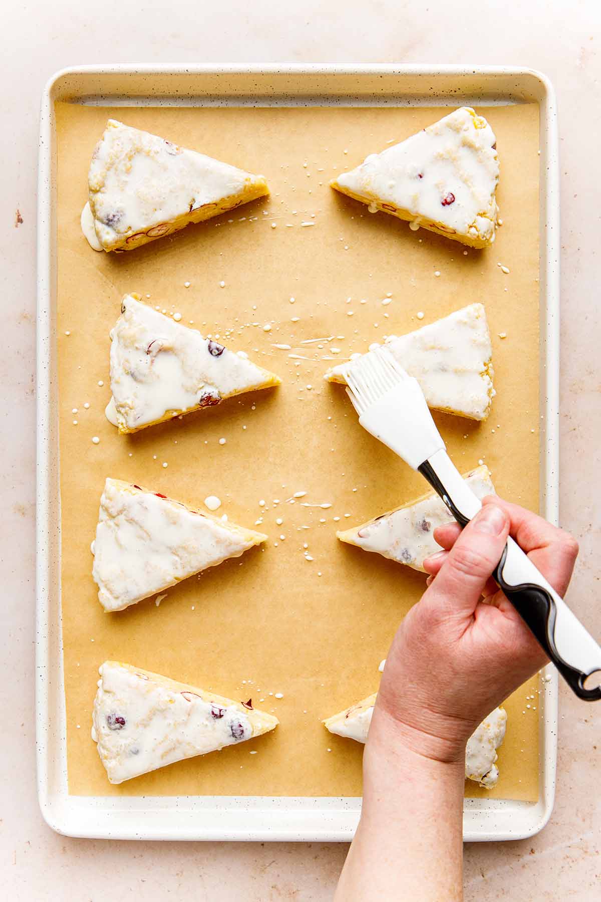 A hand brishing cream on unbaked scones.