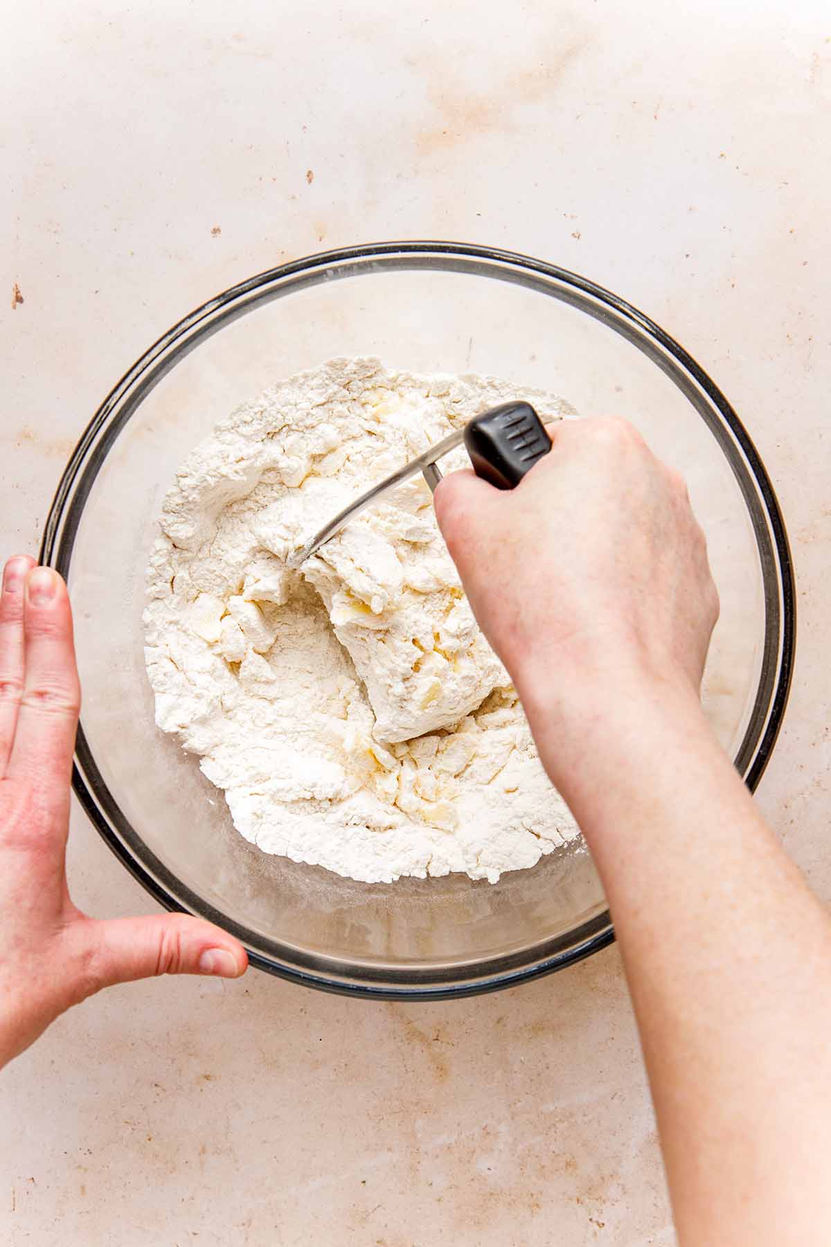 A hand using a pastry blender to cut butter into flour.
