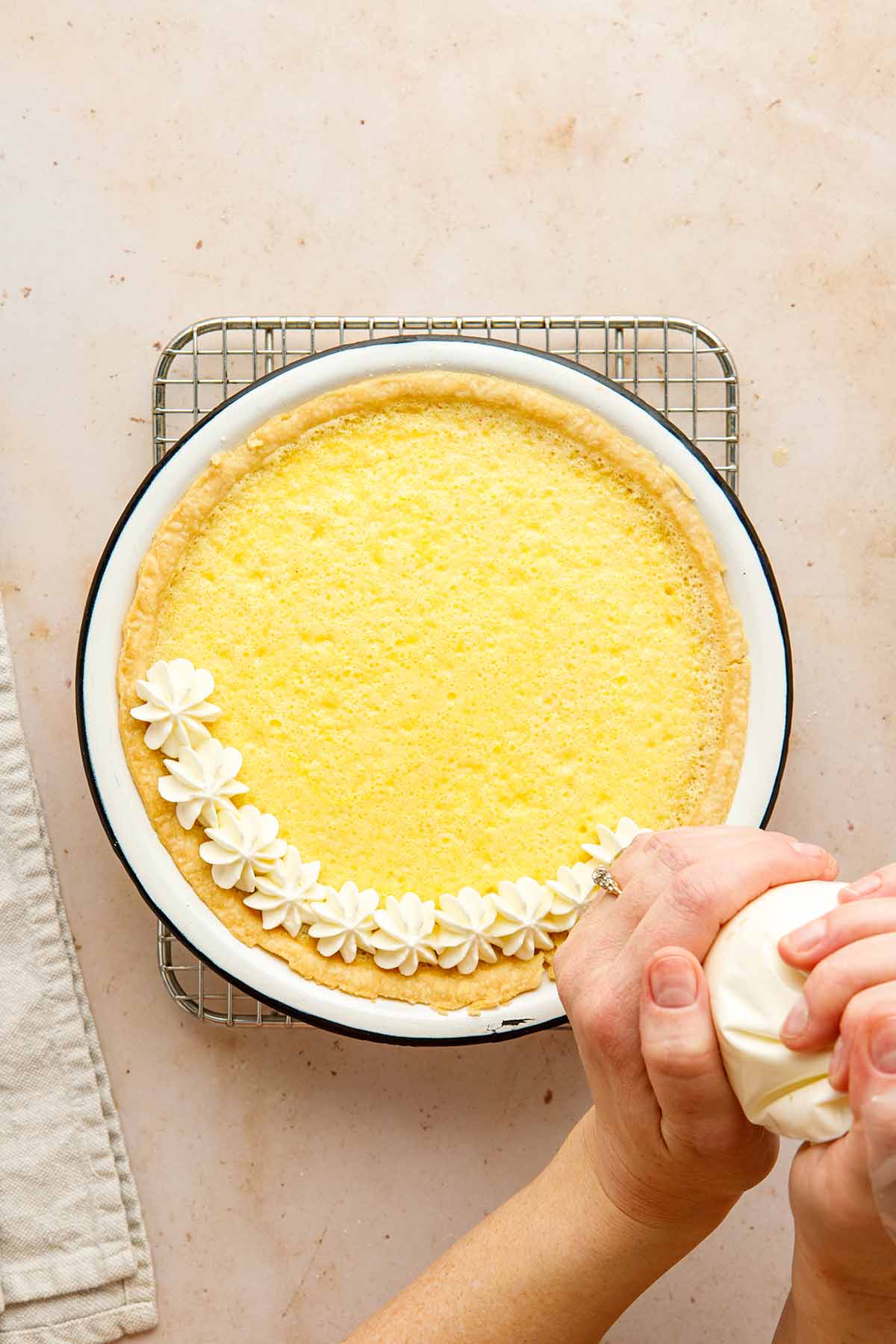 A hand piping whipped cream on top of a lemon chess pie.