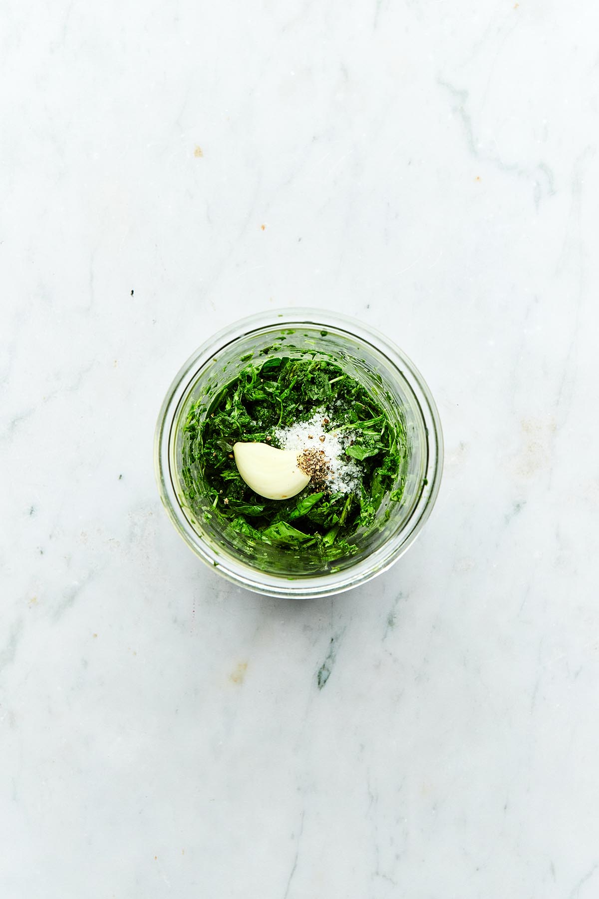 Puréed basil and spinach in a jar topped with a garlic clove, flaky salt, and cracked pepper.