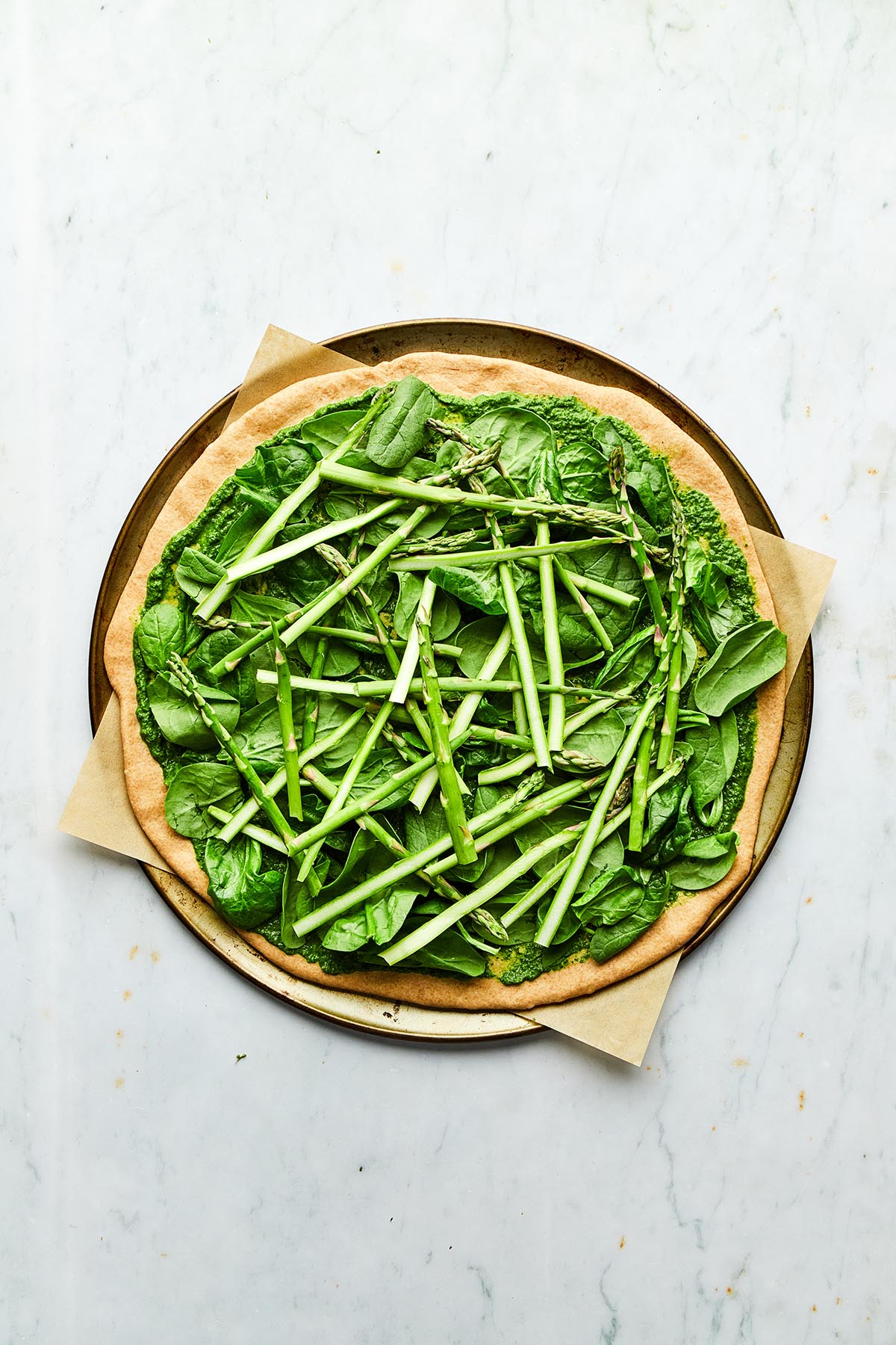 An unbaked pizza topped with spinach and asparagus.