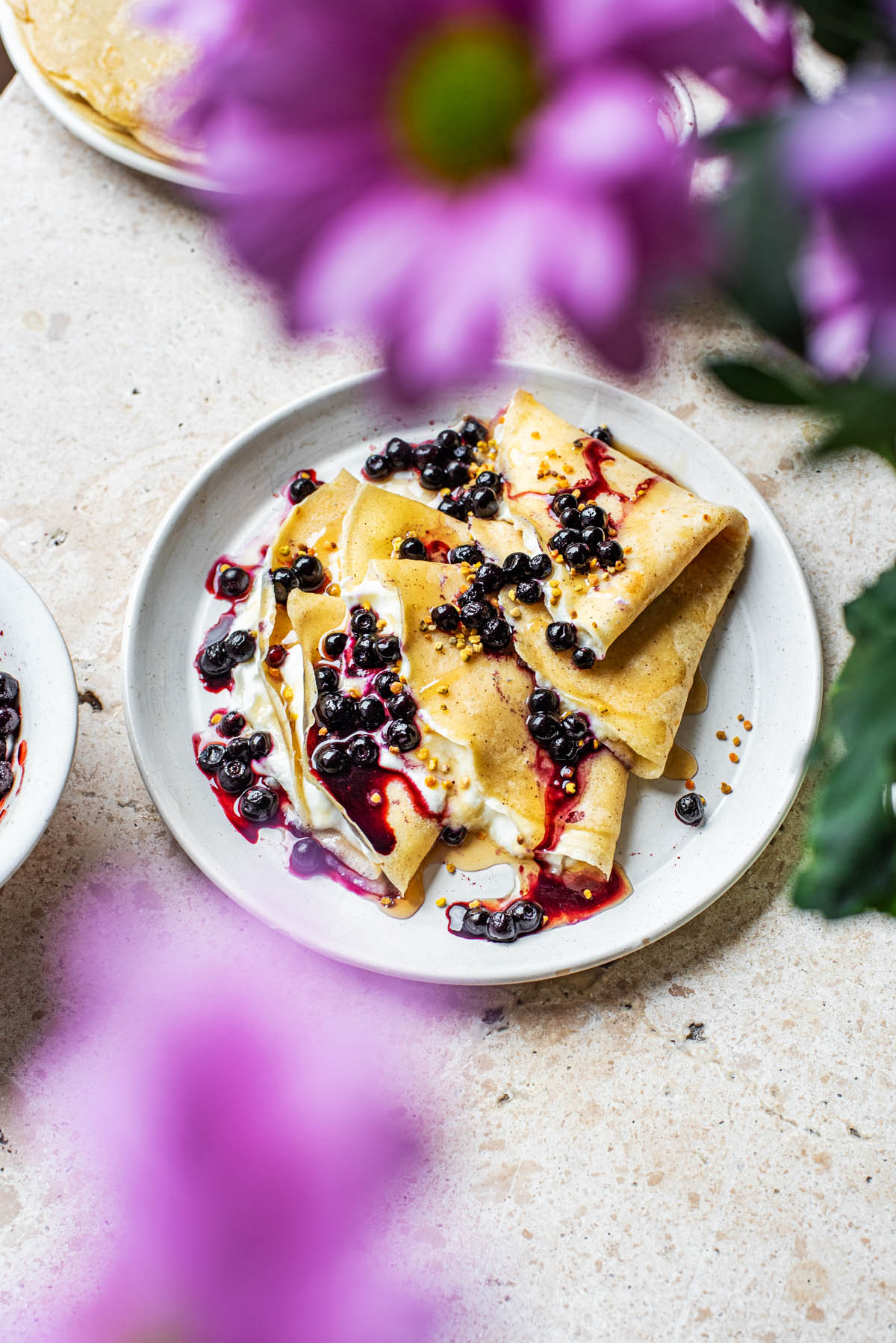 Crepes with yogurt and berries, flowers in front.
