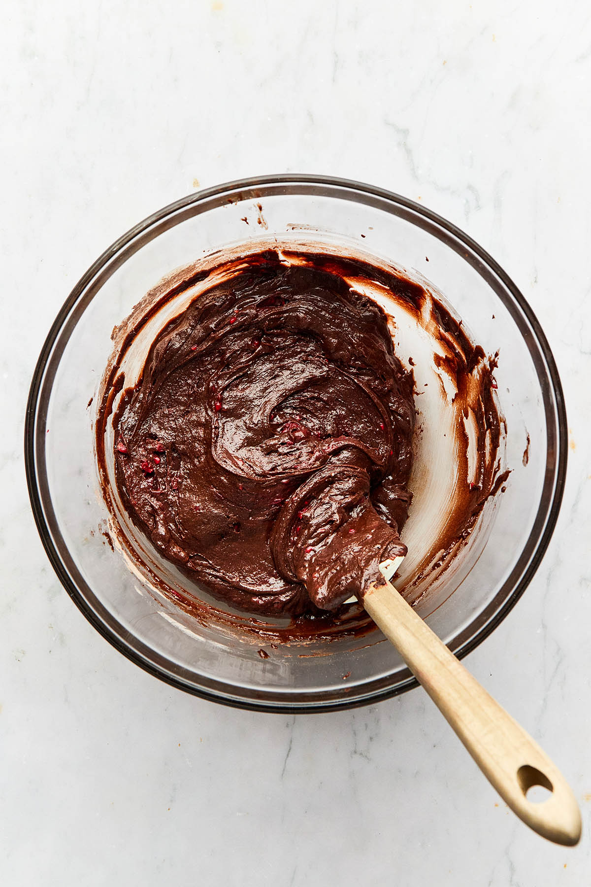 Chocolate batter in a large glass bowl with a rubber spatula inside the bowl.