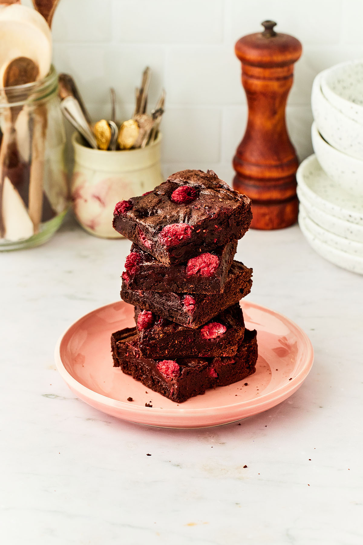 A stack of raspberry brownies on a pink plate on a marble countertop.