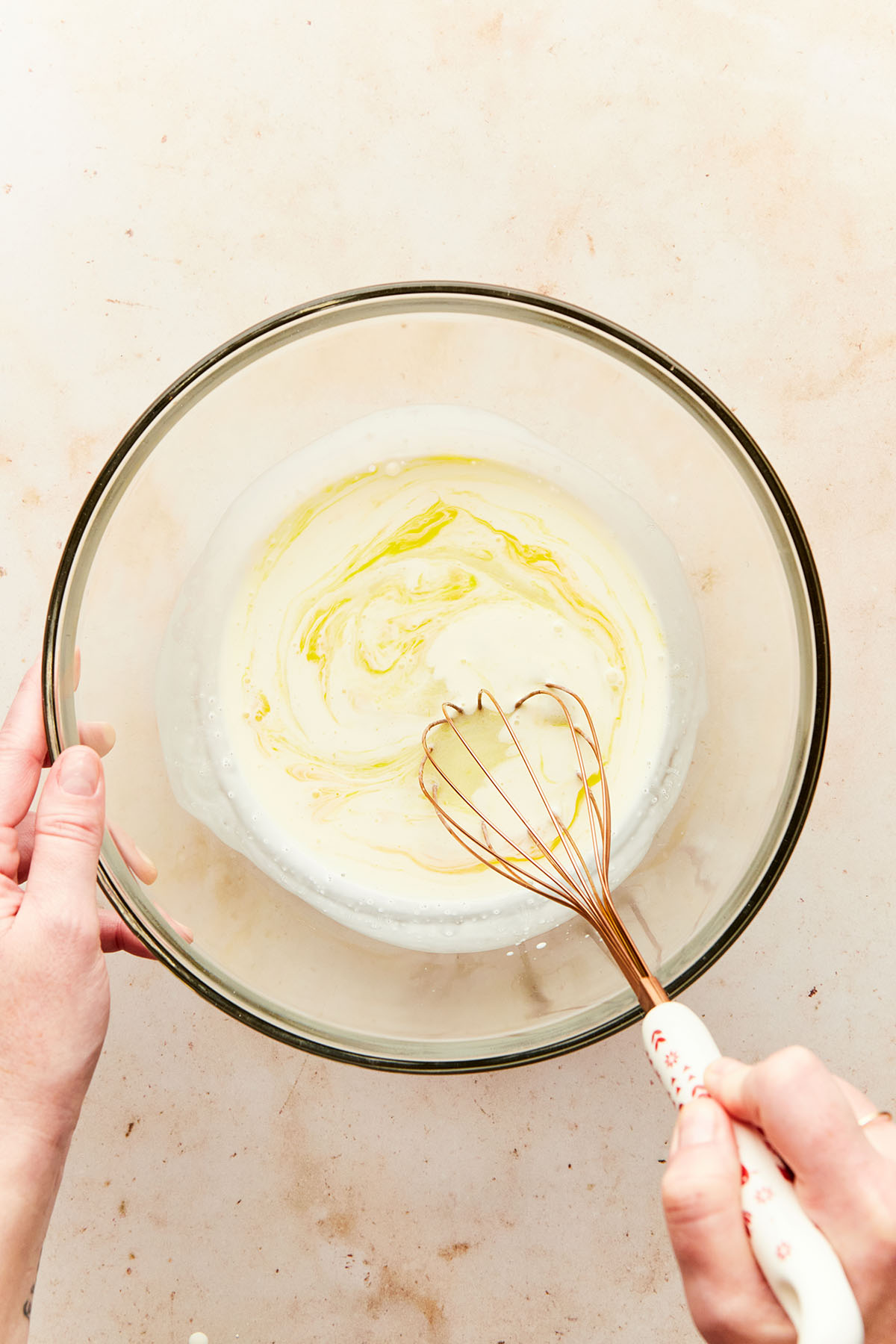 A hand whisking wet ingredients in a clear mixing bowl.