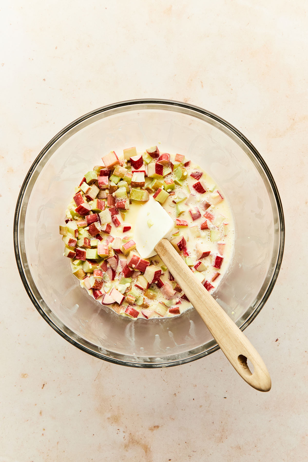 Chopped rhubarb mixed with cream, egg, sugar, and chopped ginger in a bowl.