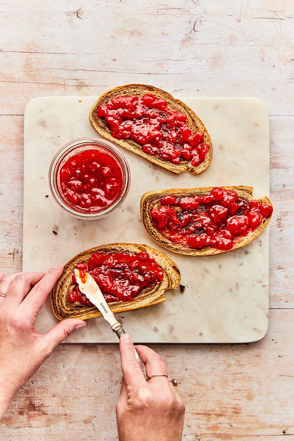 A hand spreading small-batch strawberry jam onto a slice of toast.