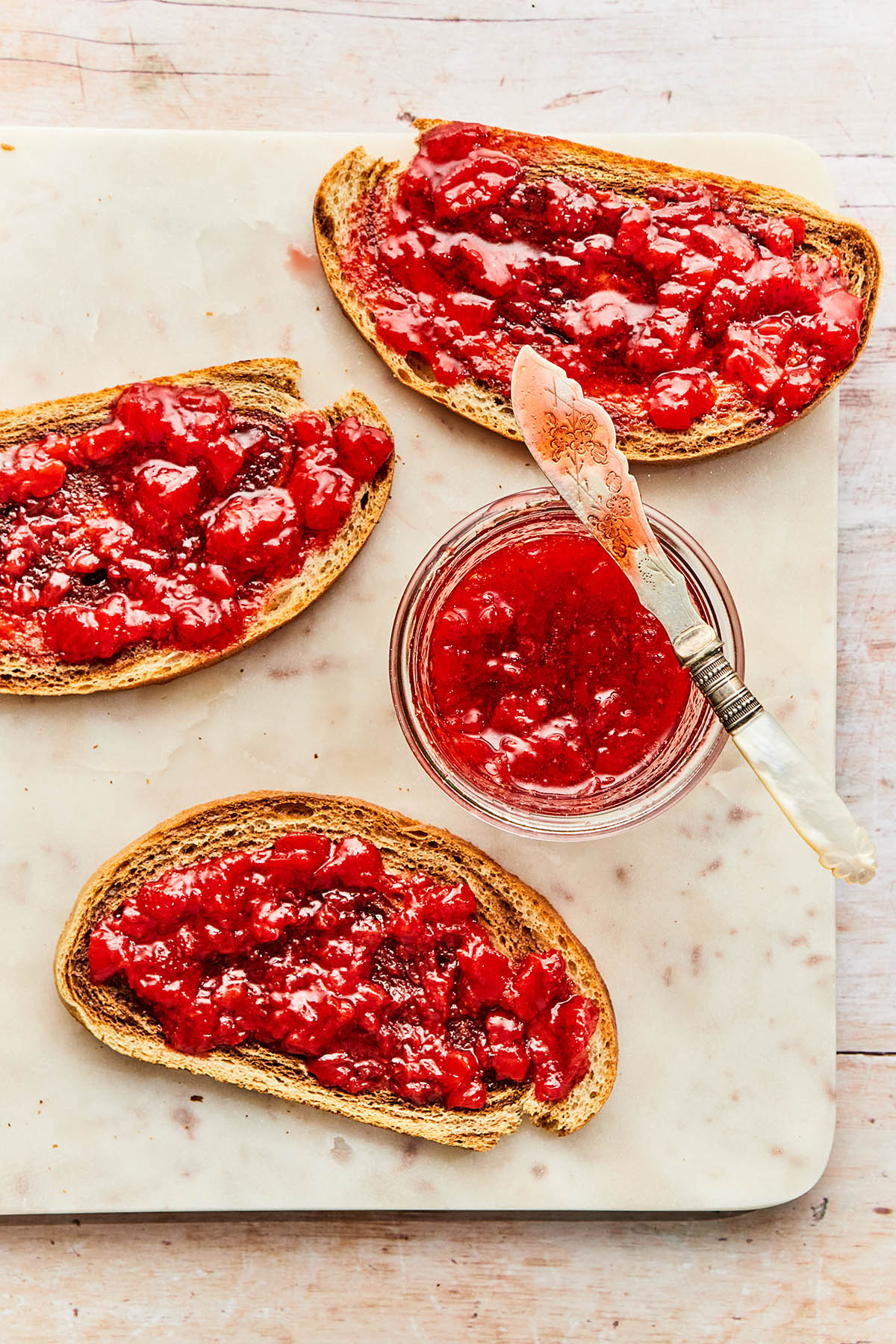 Overhead image of a jar of small-batch strawberry jam alongside slices of toast with jam.