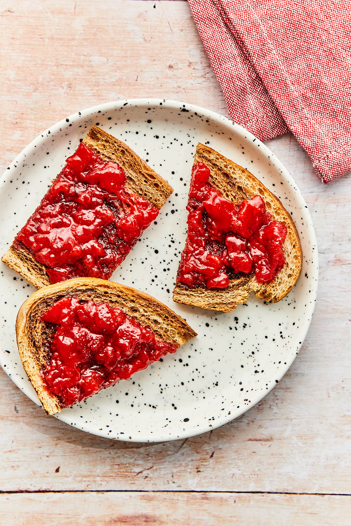 Sliced toast topped with small-batch strawberry jam on a small white-speckled plate.
