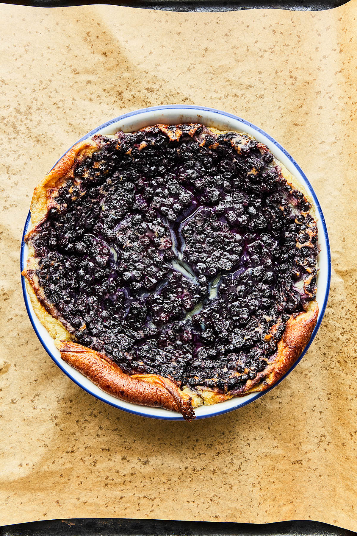 A whole baked blueberry clafoutis on a parchment paper-lined baking sheet.