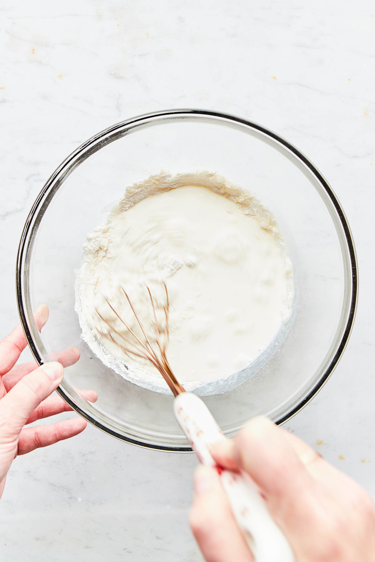 A hand using a whisk to mix ingredients in a glass bowl.