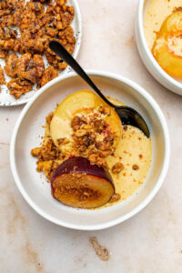 A bowl of baked stone fruit topped with vanilla custard and candied walnuts.