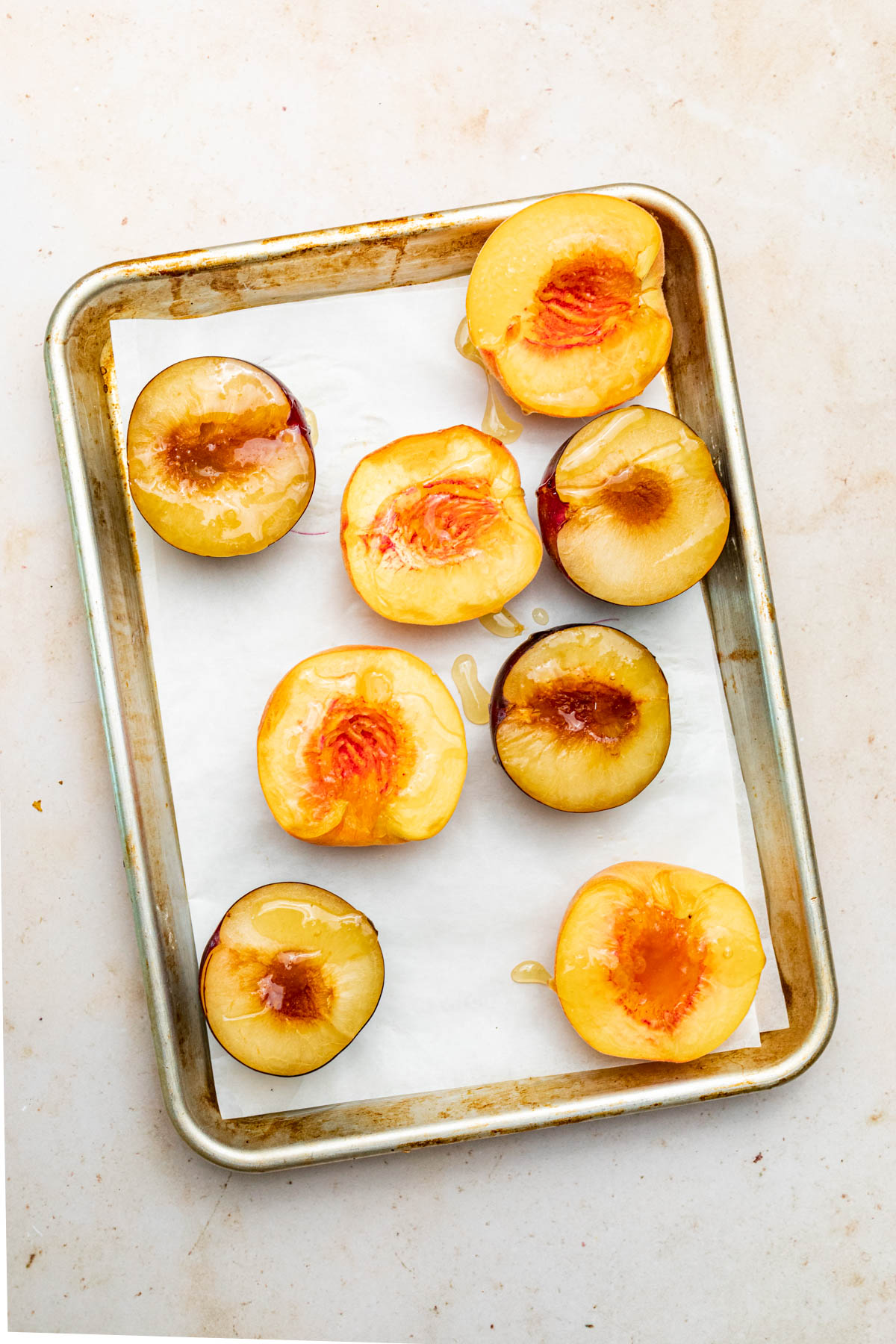 Halved peaches and plums drizzled with honey on a baking sheet.
