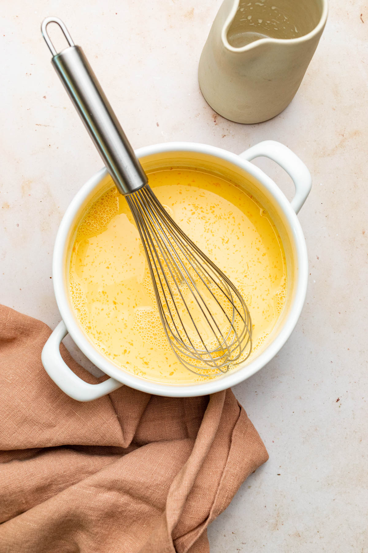 A white dish of custard with a whisk resting inside the dish.