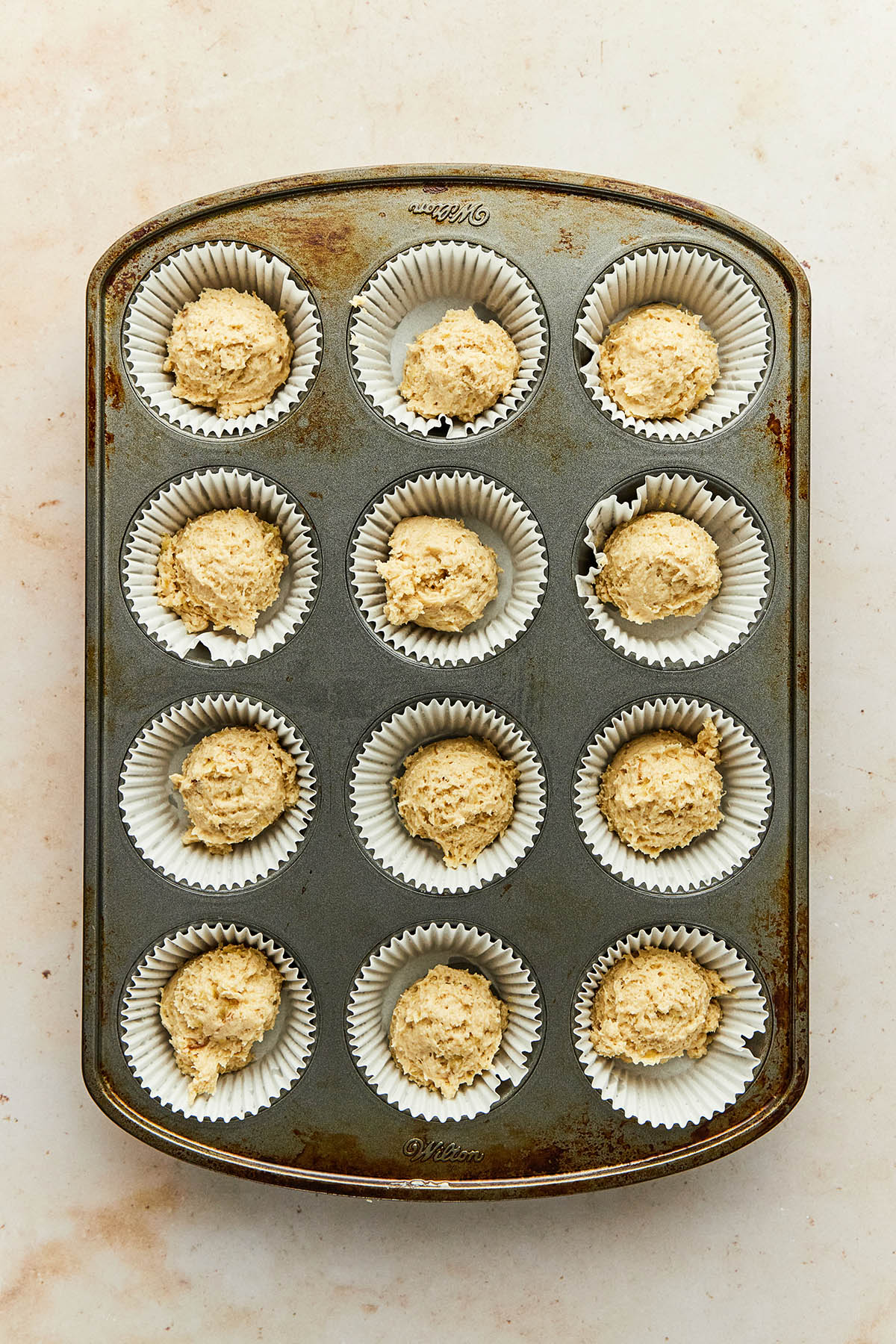 Scoops of banana muffin batter in a metal muffin tin lined with paper cupcake wrappers.