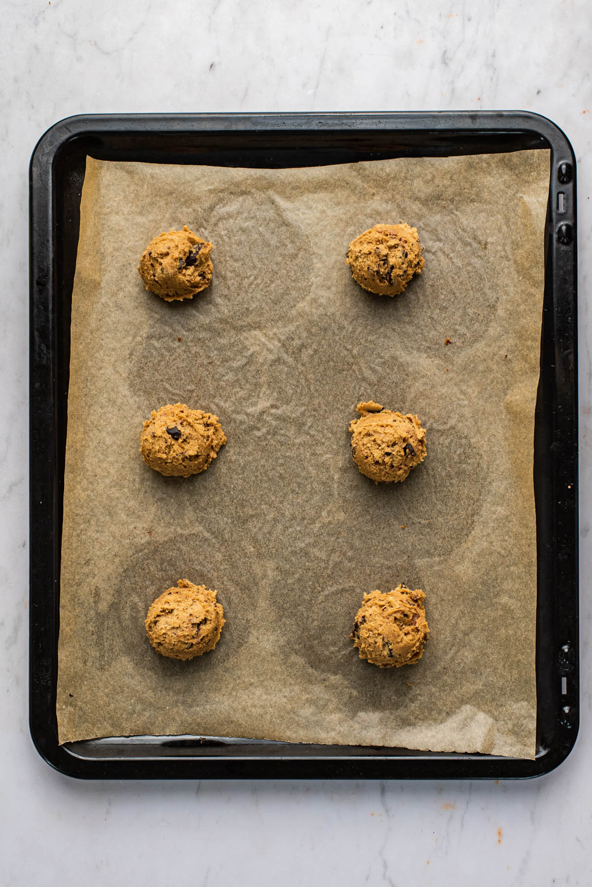 Six scoops of cookie dough on a lined baking sheet.