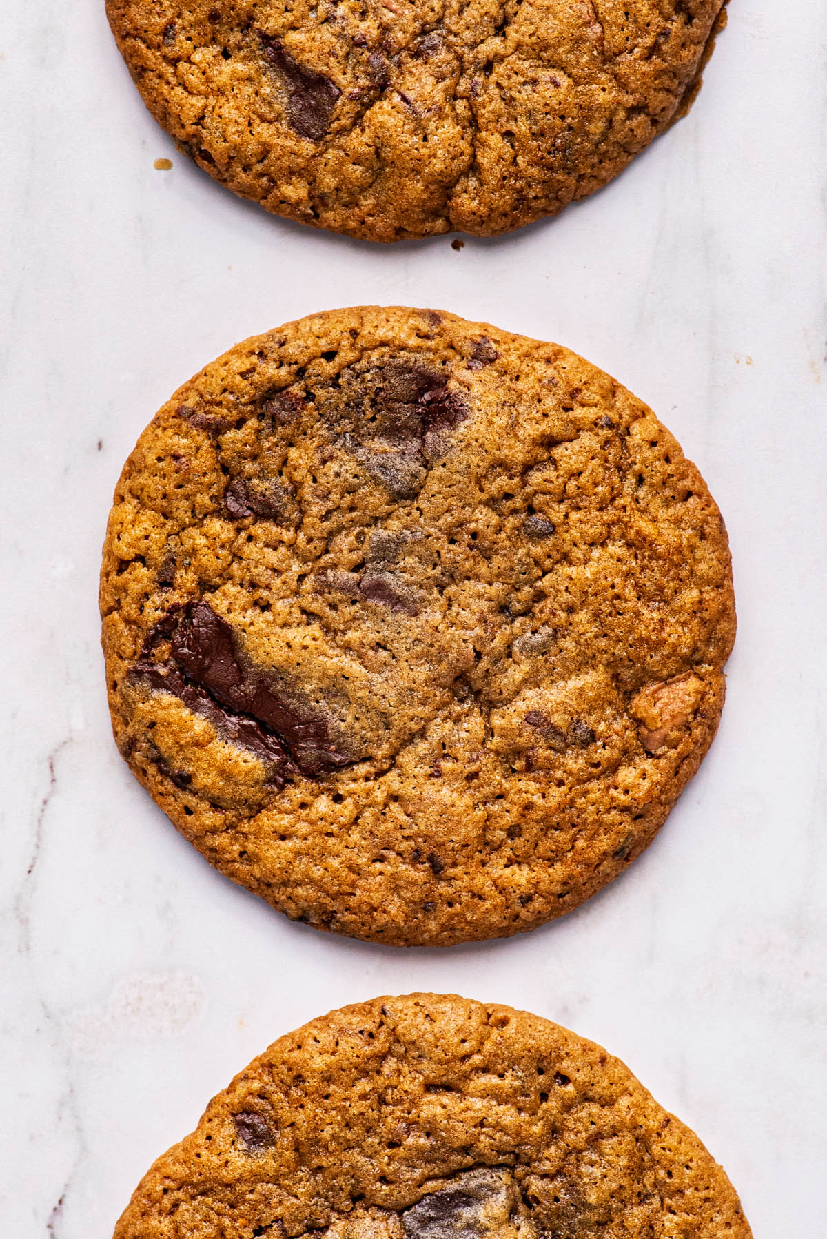 Three large chocolate chunk cookies arranged in a row.