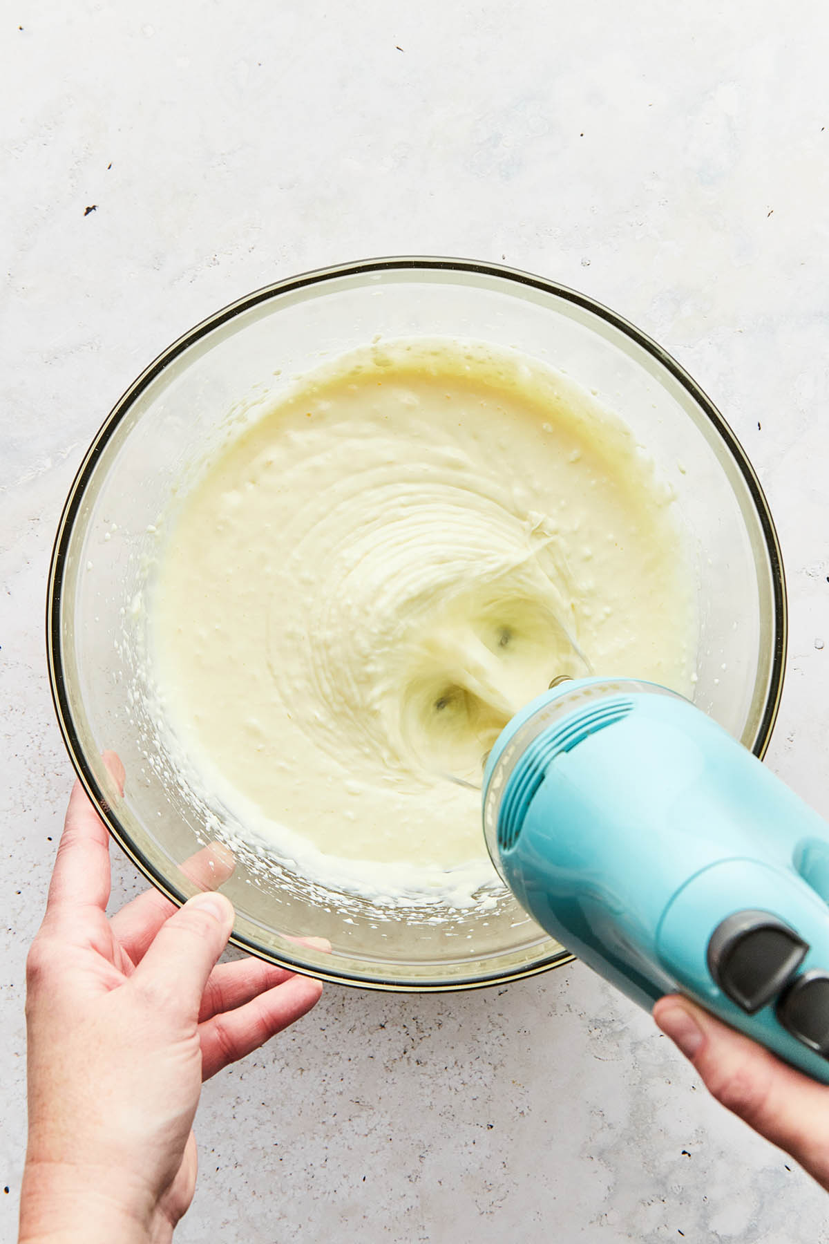 A hand using a handheld mixer to whip gluten-free cheesecake filling.
