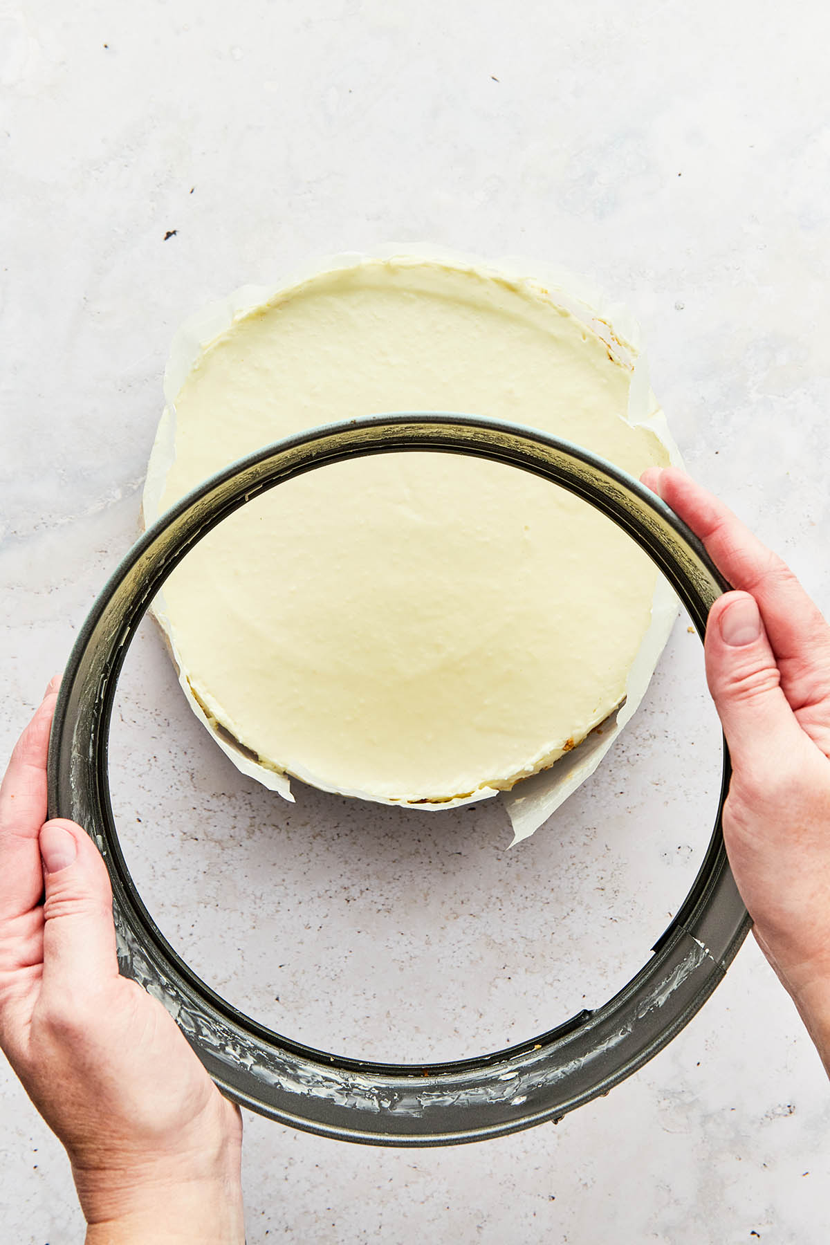 Hands removing the metal collar of a springform tin from a cheesecake.