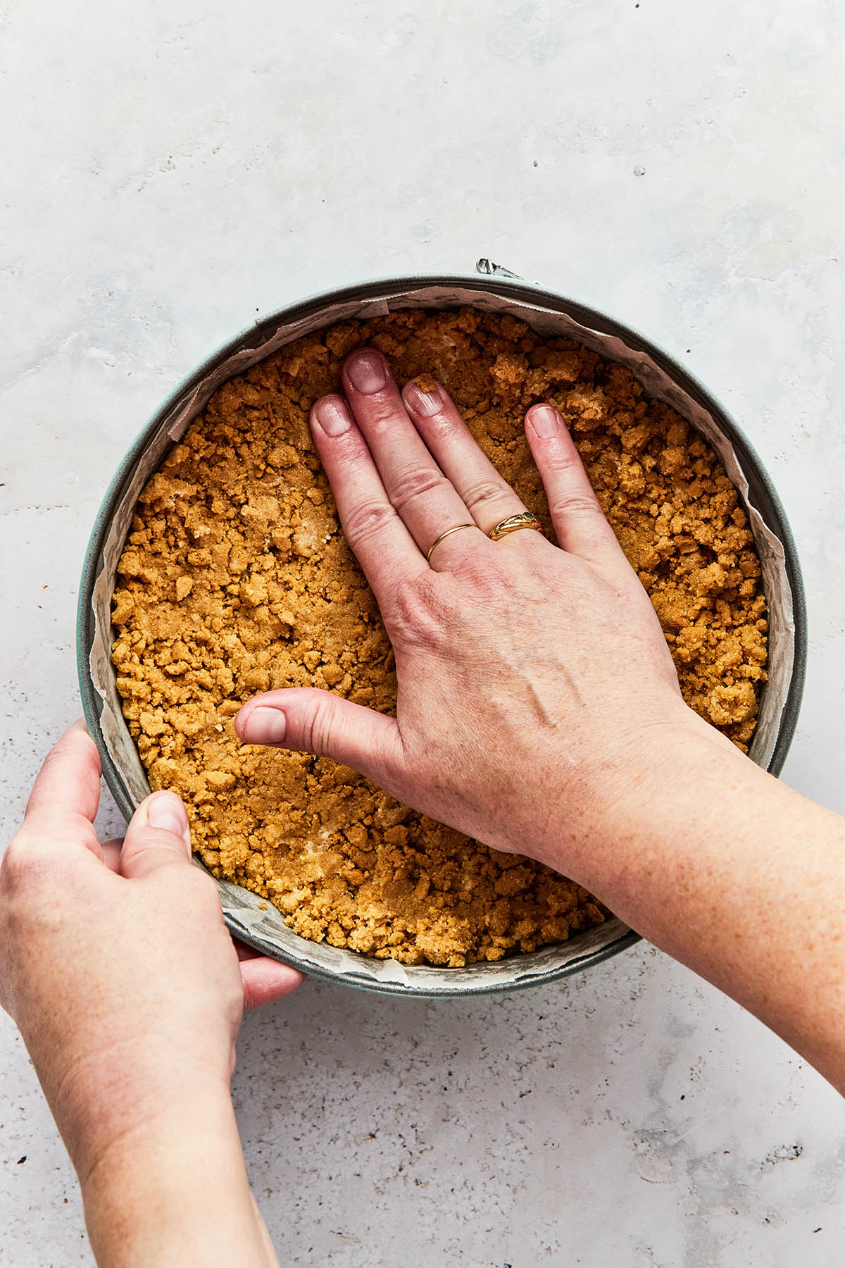 A hand pressing gluten-free cheesecake crust into an even layer inside a springform tin.