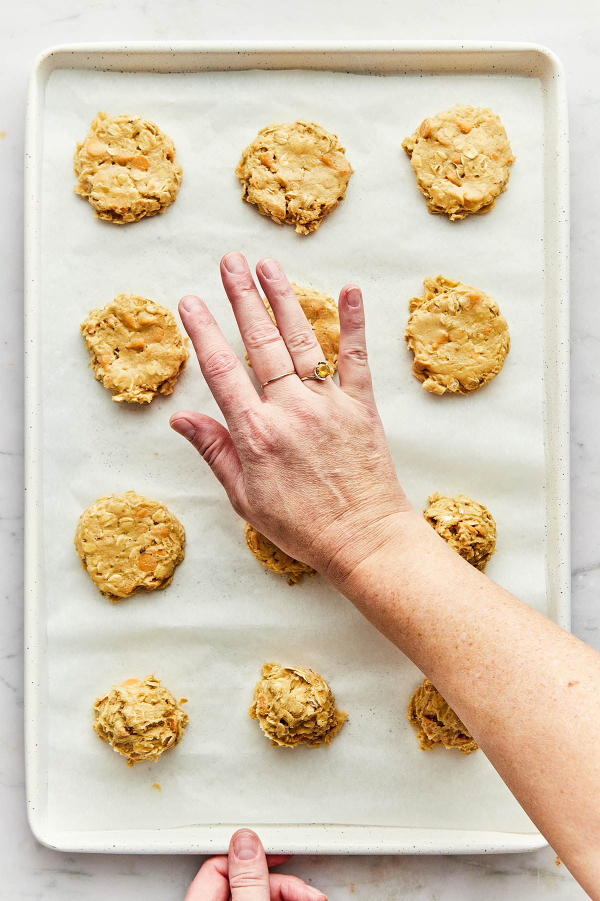 A hand flattening scoops of cookie dough on a baking sheet.