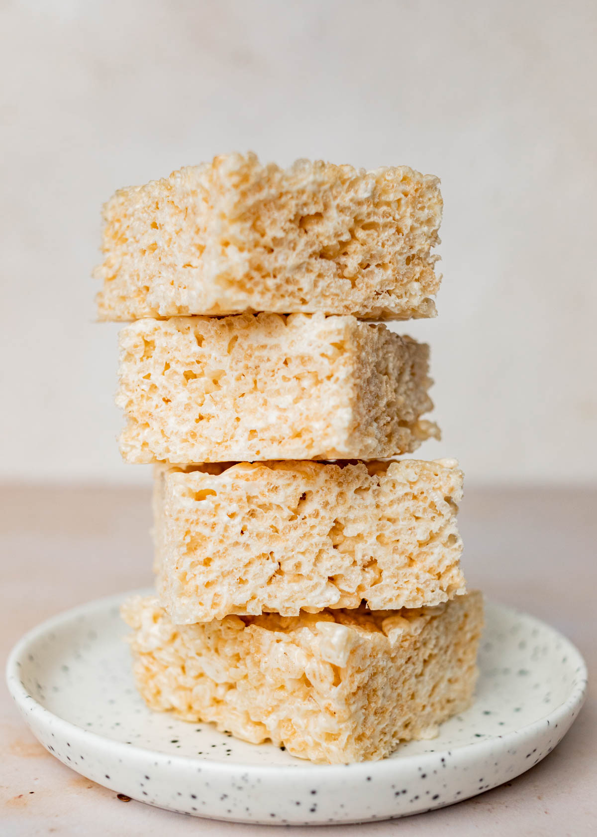 A front-on image of four Rice Krispie treats stacked on a small white speckled plate.