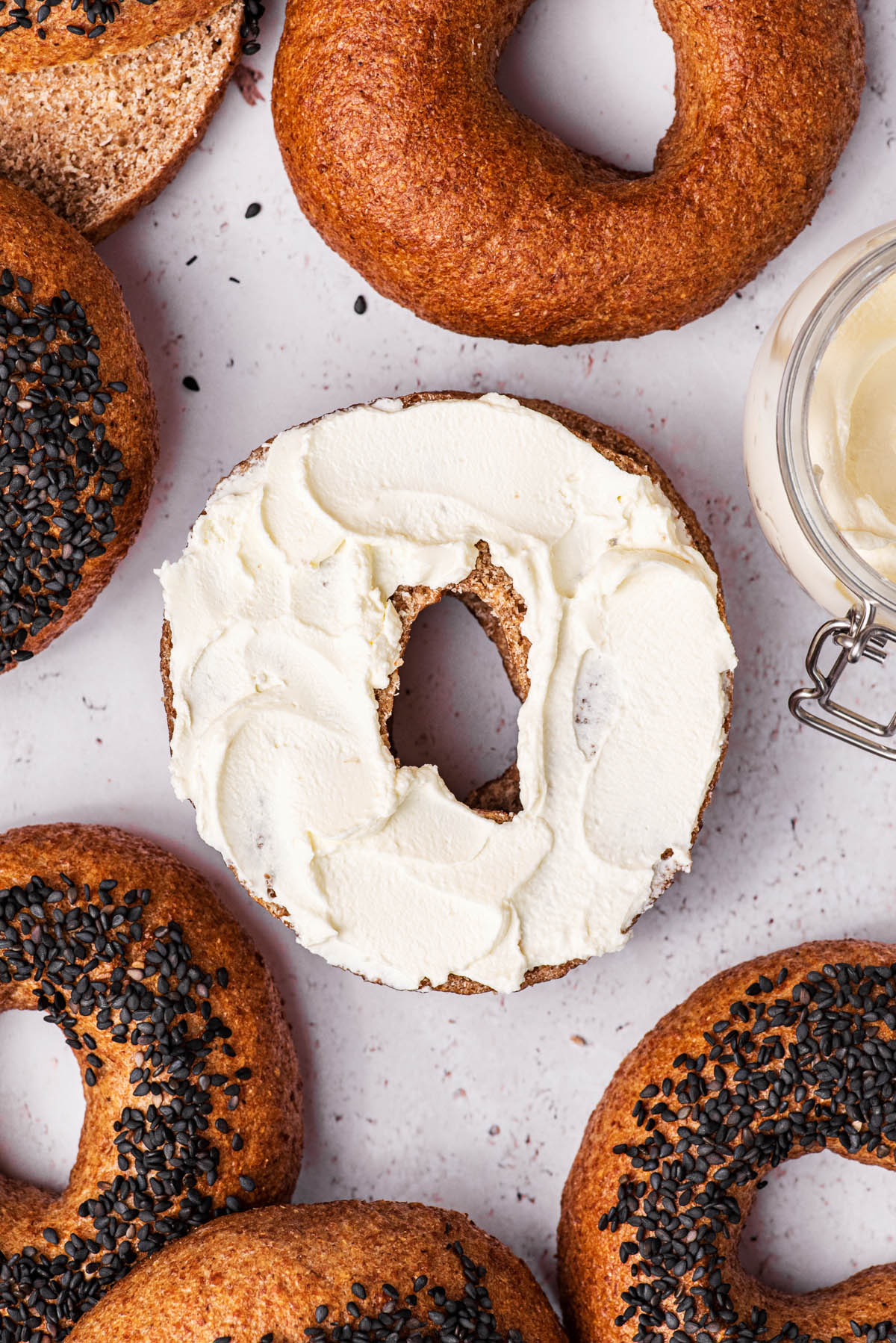 Several bagels, some topped with black sesame seeds, one half with cream cheese.