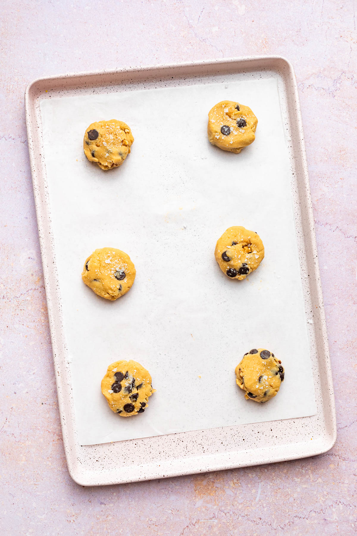 Six portions of unbaked cookie dough on a parchment paper-lined baking sheet.