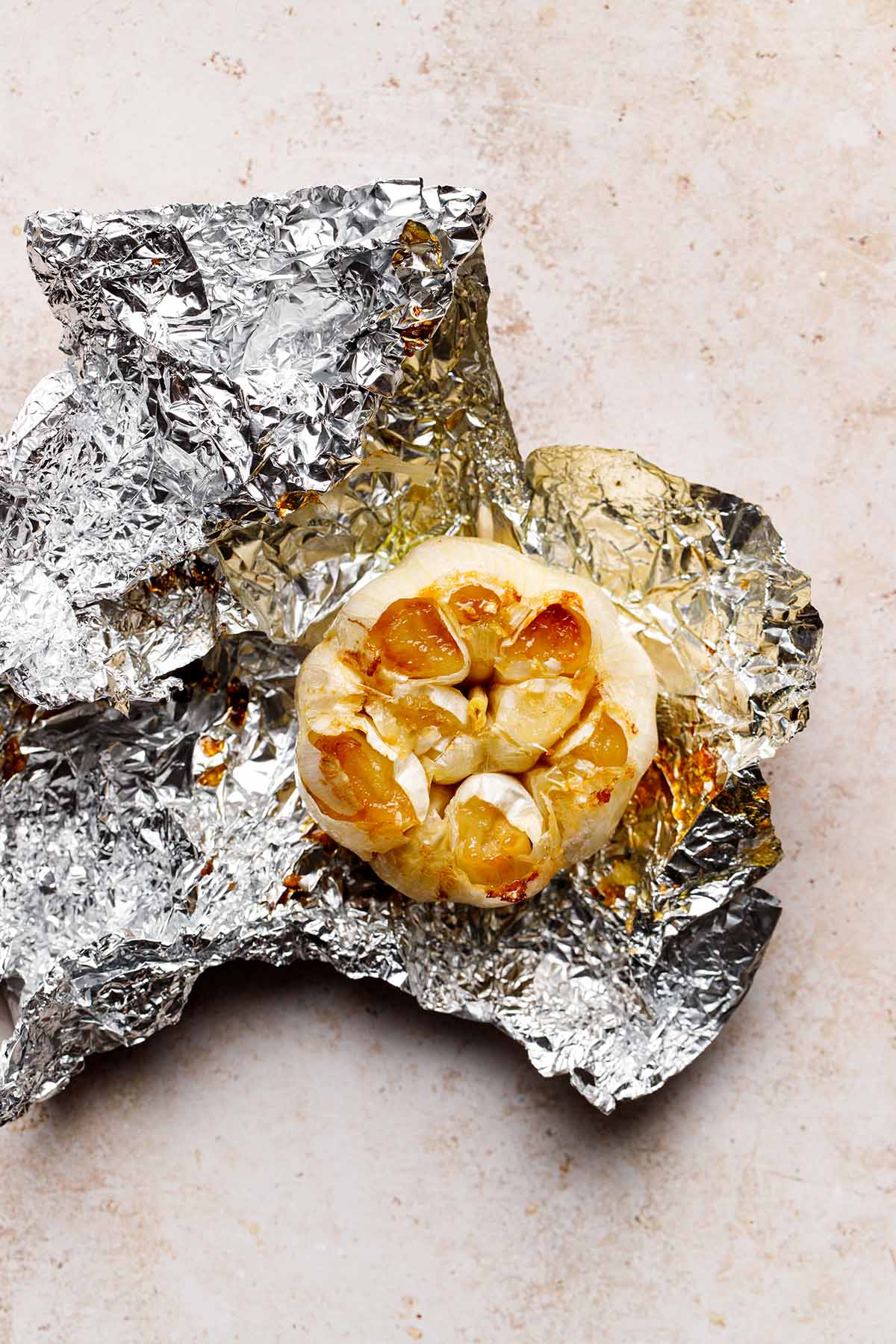 A bulb of cooked garlic sitting on crumpled aluminium foil.