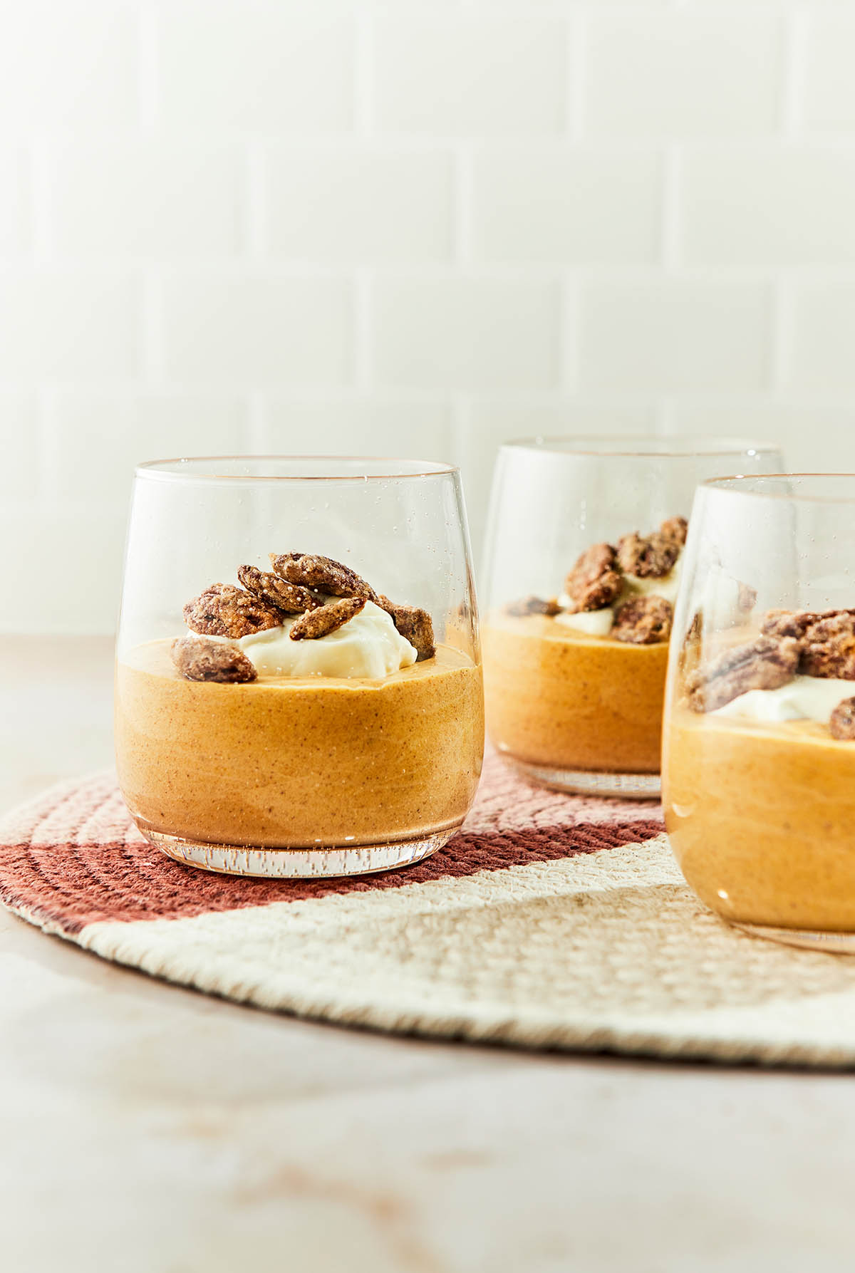 Straight on shot of three dishes of pumpkin mousse on a round placemat on a stone surface with a tiled background.