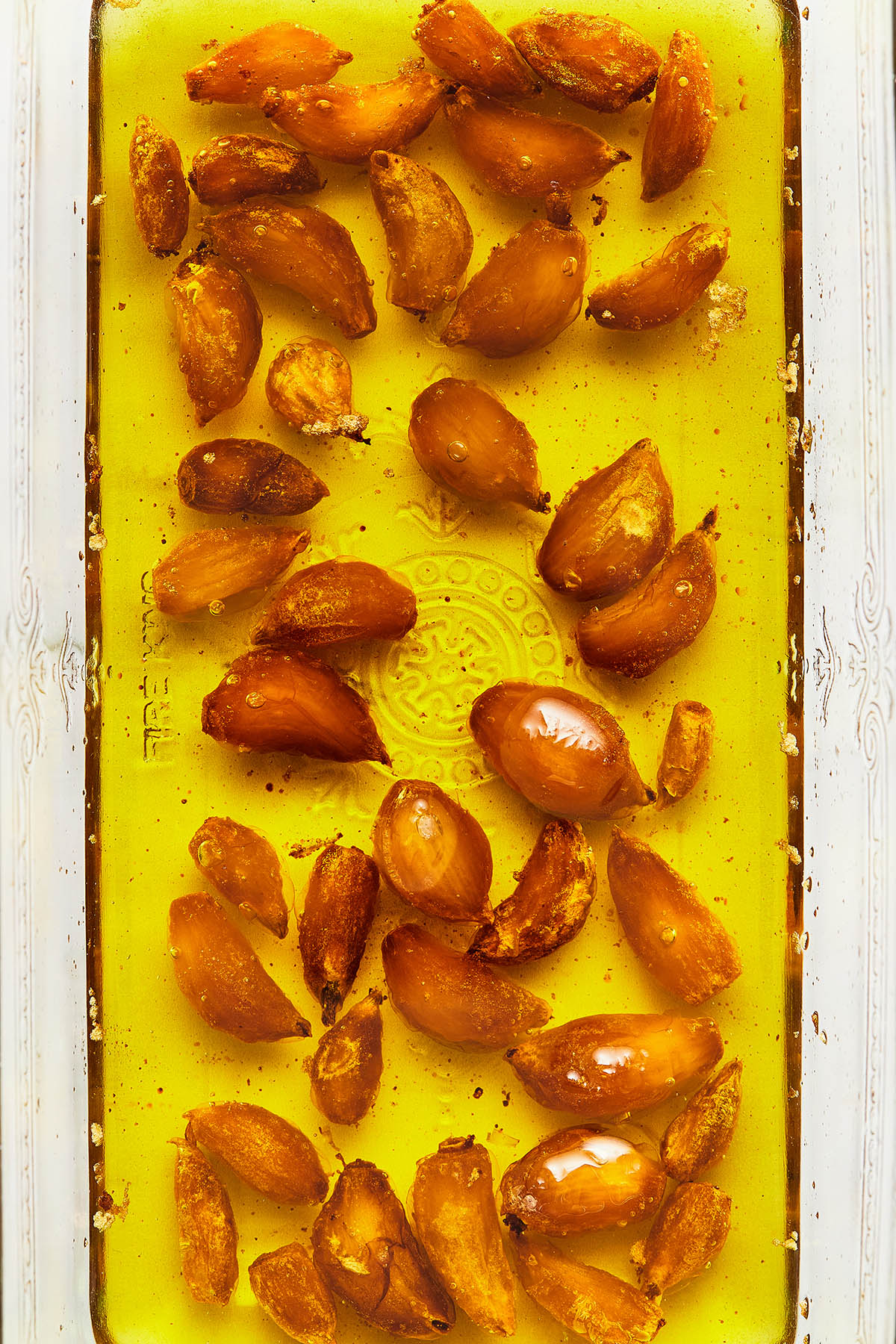 A glass loaf tin of roasted garlic cloves covered in oil for a post called How To Roast Garlic..