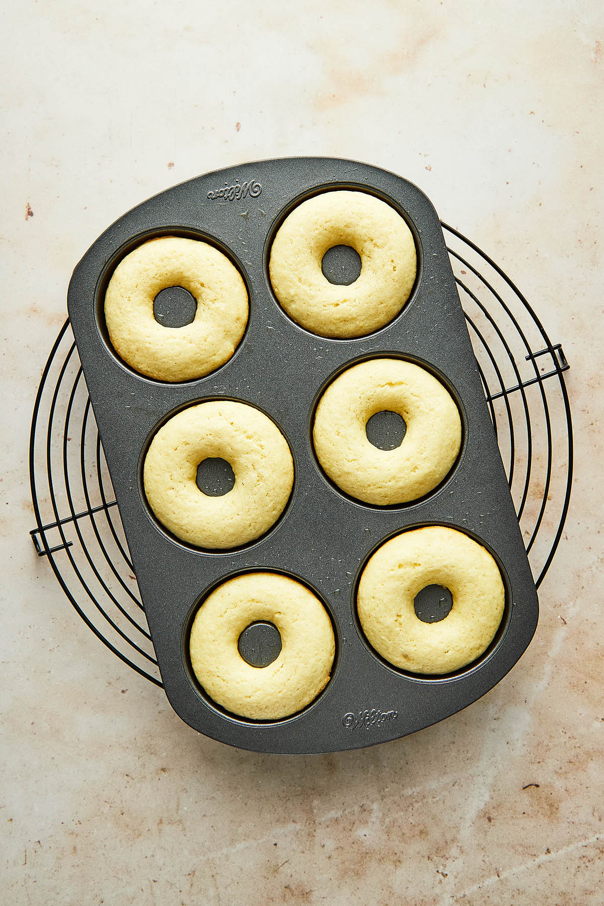 A tin of six baked donuts on a cooling rack.
