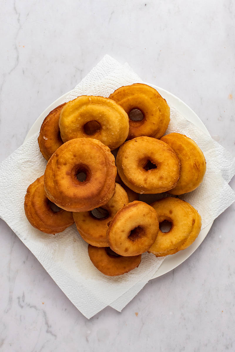 Donuts cooling on a paper towel lined plate.