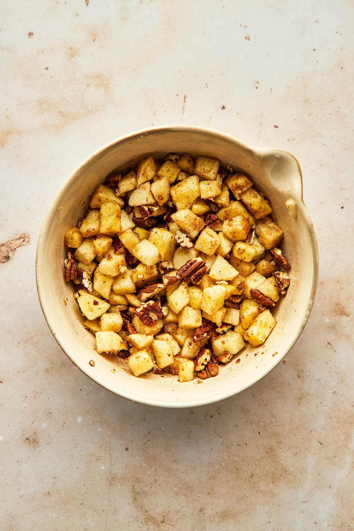 A bowl of diced apples stirred with pecans, cinnamon, and sugar.