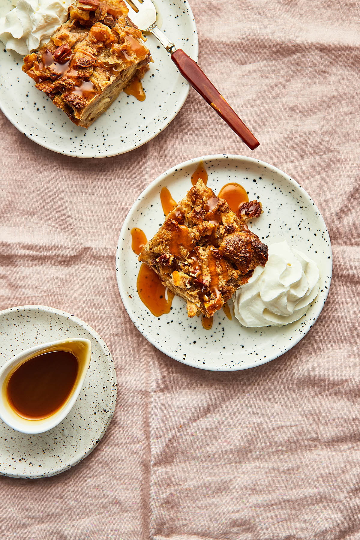 Two small plates of croissant bread pudding with whipped cream and caramel sauce.