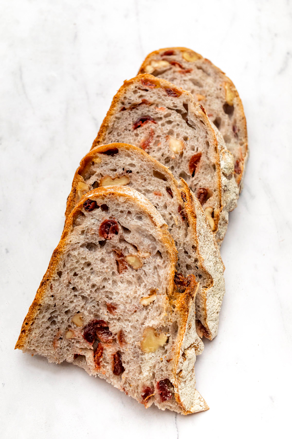 Close up of slices of cranberry sourdough bread, stacked together, but laying down on a marble surface.