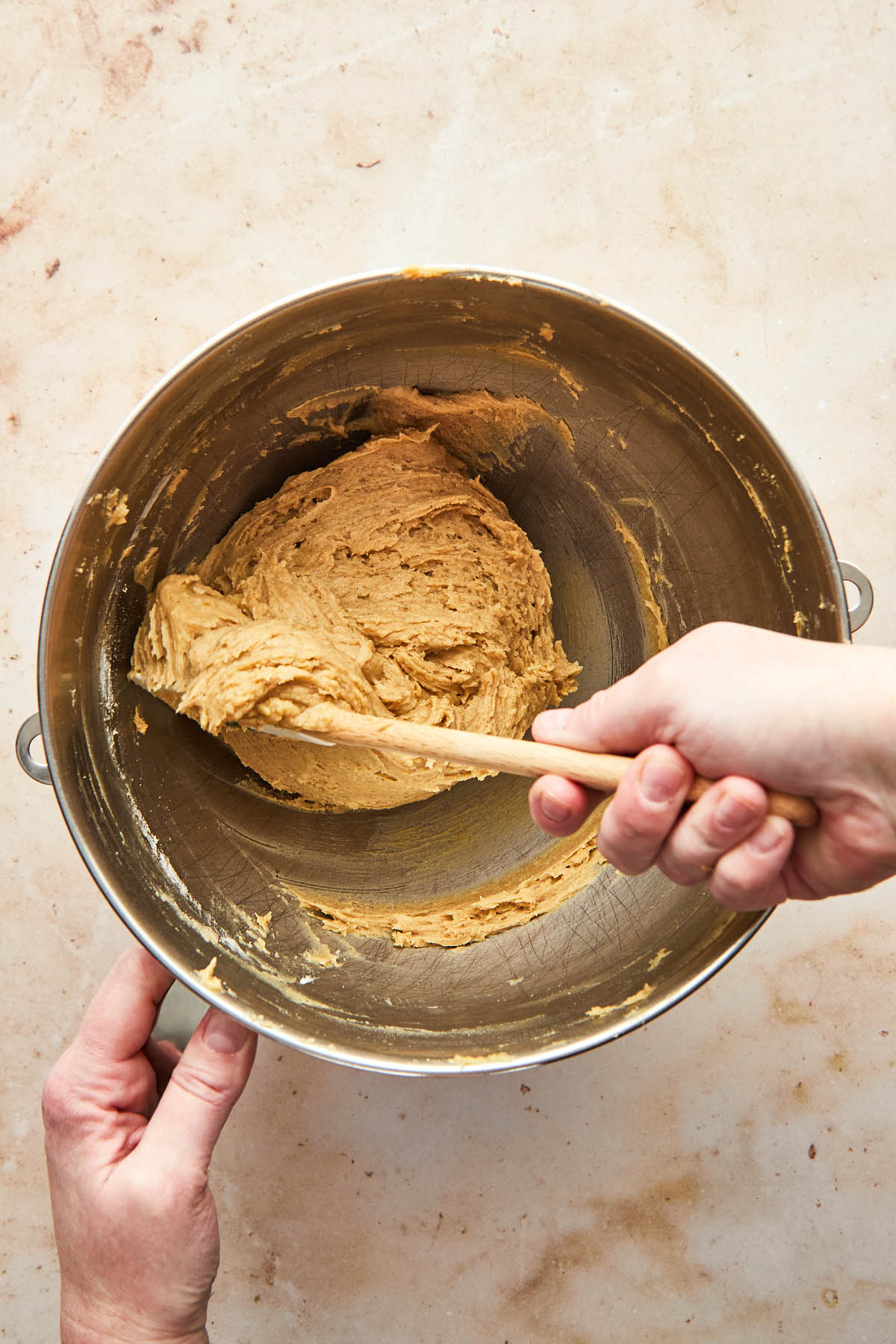 A hand stirring cookie dough in the bowl of a stand mixer.